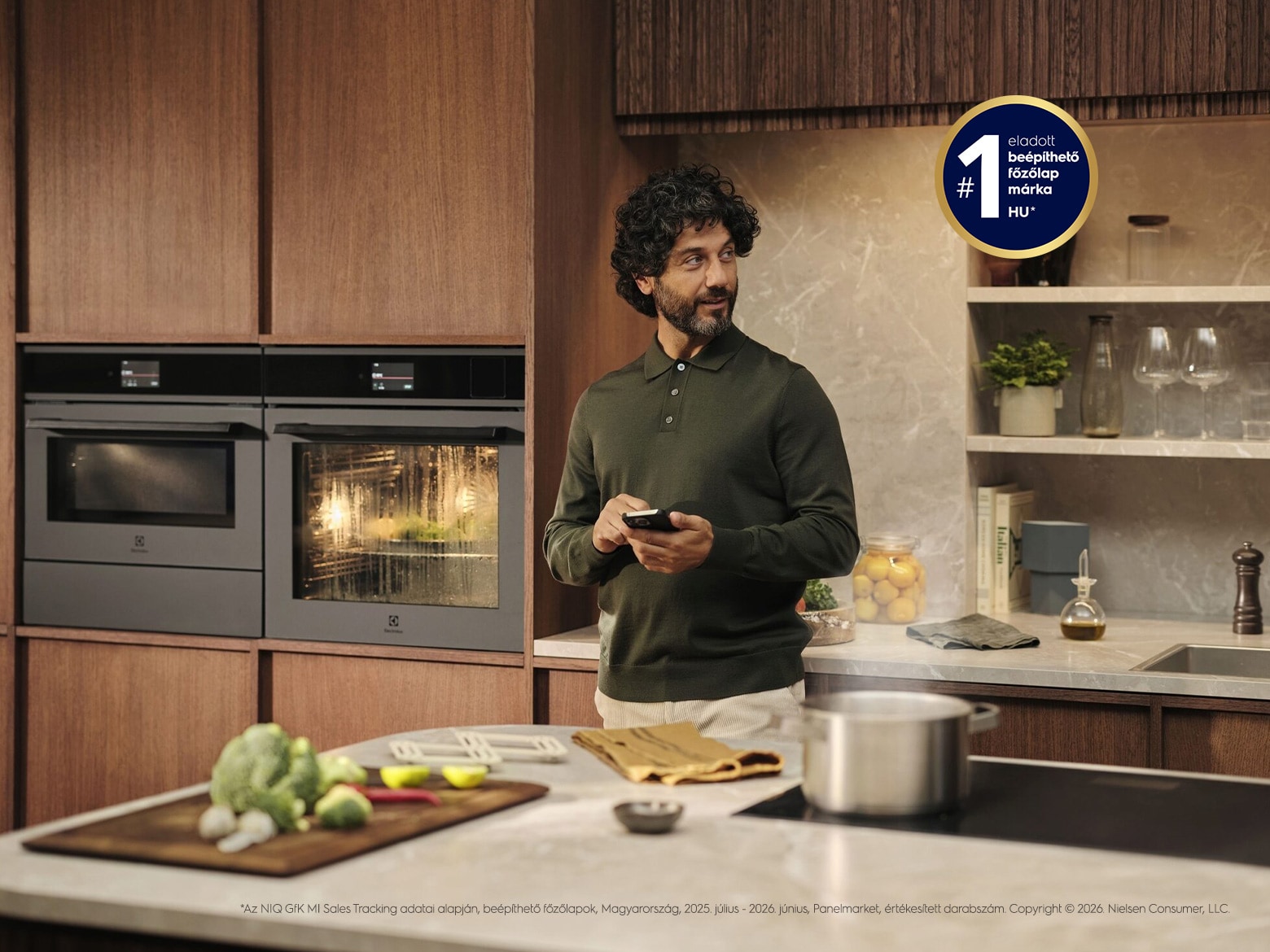 A man is holding his mobile phone while standing in front of the kitchen counter.