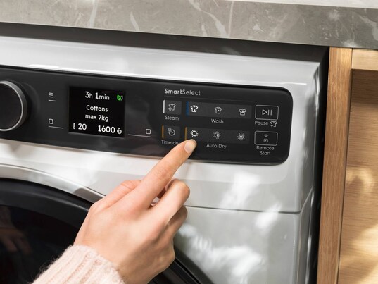 A woman pressing the control panel on a washer dryer.