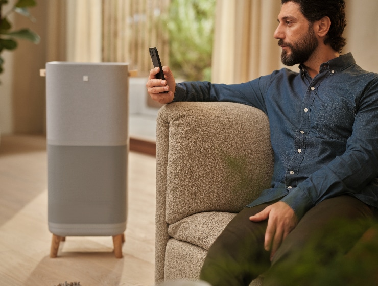 Férfi telefont tart a kezében, és egy légtisztító mellett ül.