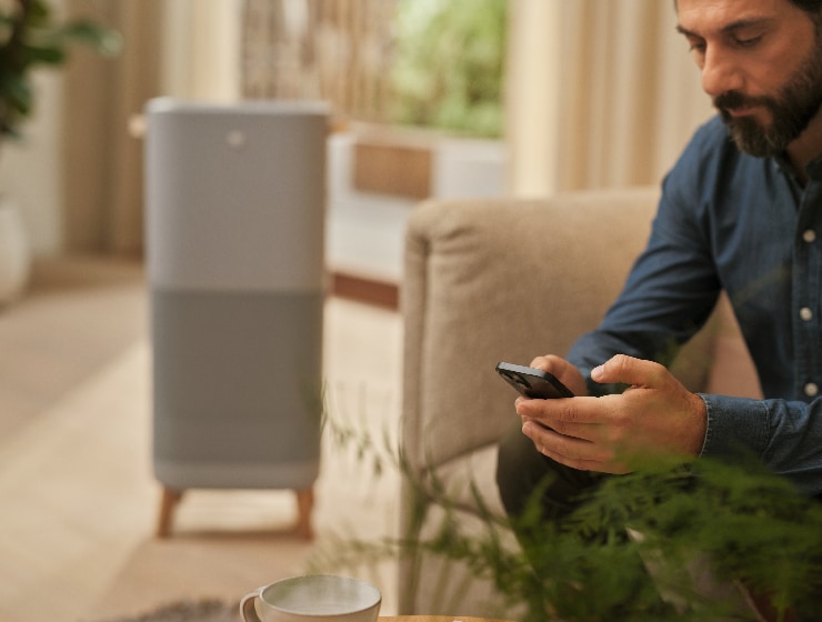 Férfi telefont tart a kezében, és egy légtisztító mellett ül.