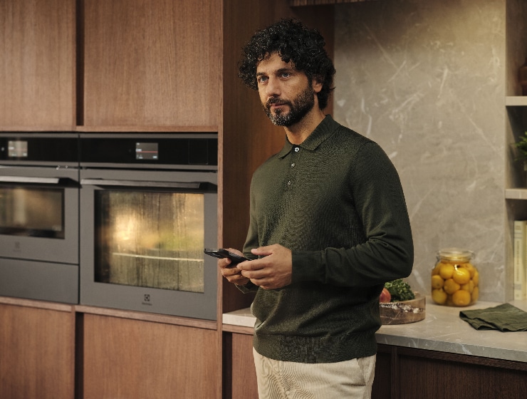 Férfi áll a konyhában, kezében telefon.