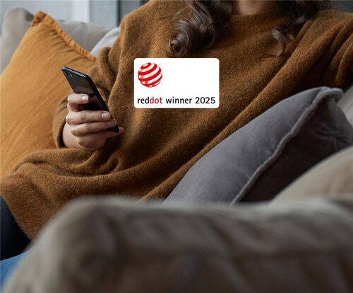 Egy nő ül a kanapén mobillal. A képen Red Dot Design logó látható.