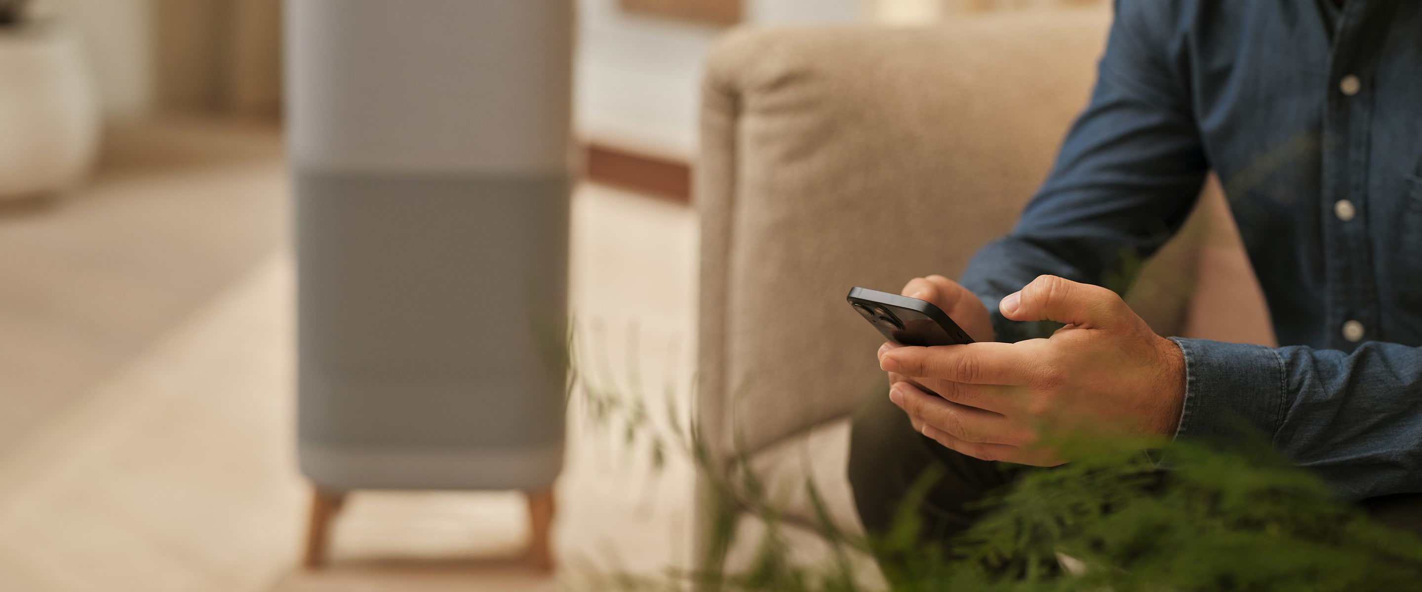 Telefonját tartó férfi ül. Légtisztító a háttérben.