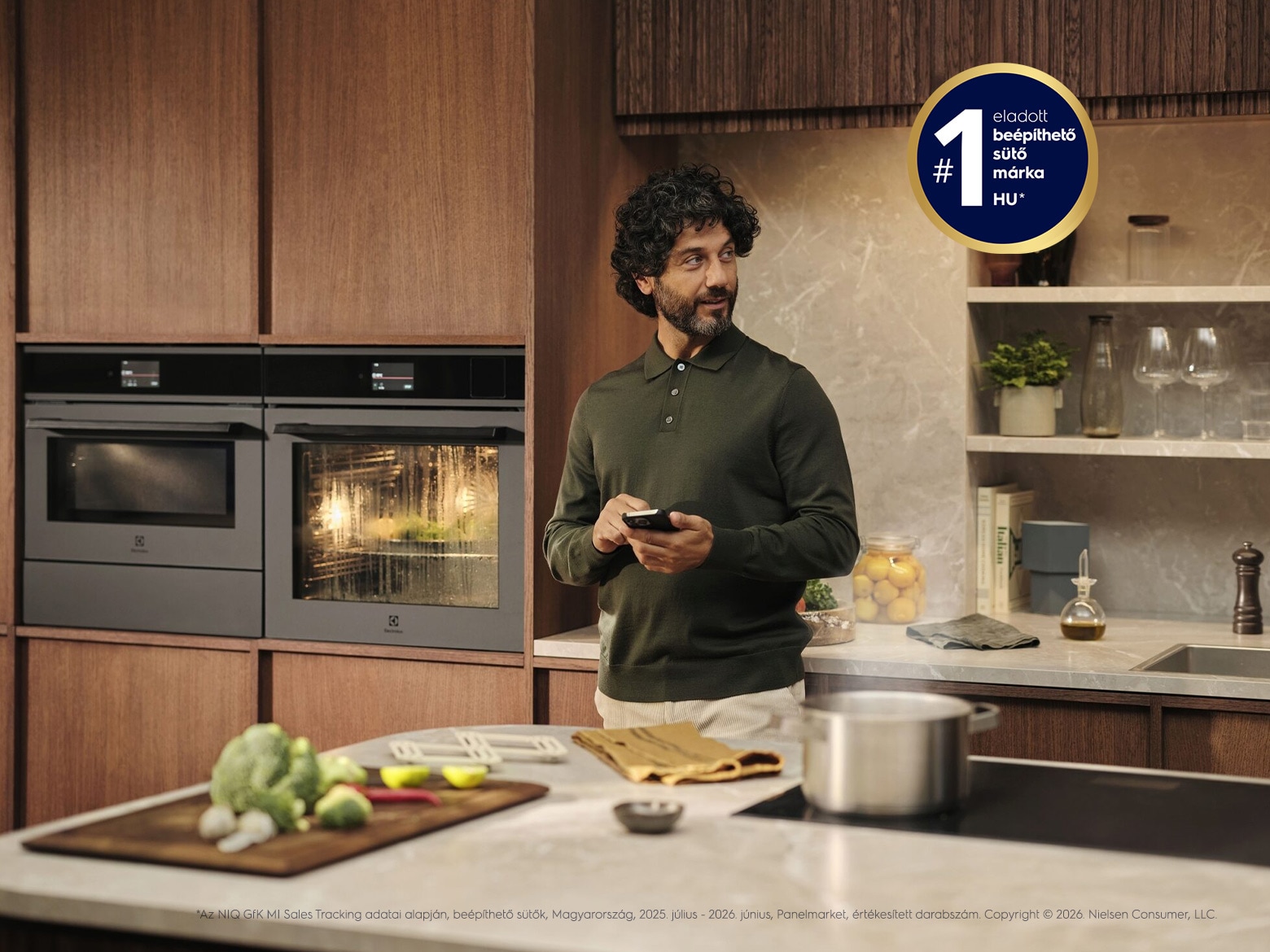 A man is holding his mobile phone while standing in front of the kitchen counter.